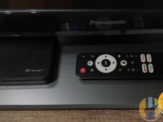 Real Android TV set-top box (Tracer) and Google Assistant remote on a Panasonic TV stand — everyday Android TV living-room kit; no forged BBC logos.