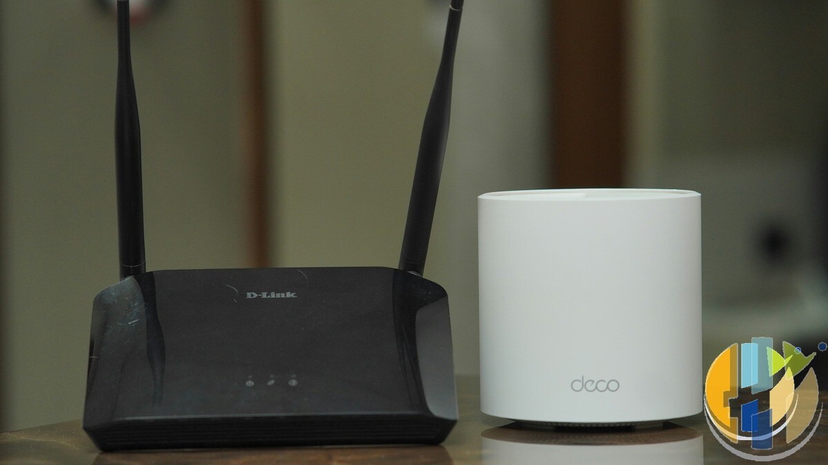Home networking vanity shot: traditional dual-antenna Wi-Fi router beside a modern mesh node on a wooden desk — multi-gig router kit vs everyday streaming gear.