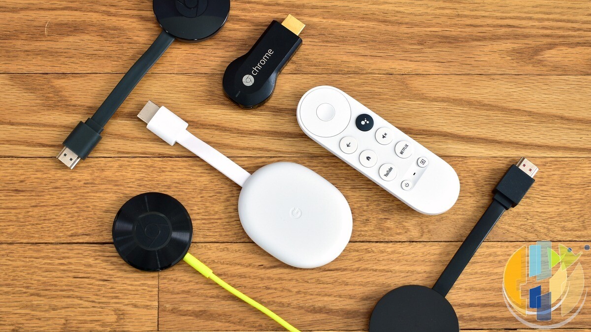 Real collection of Chromecast streaming sticks and a Google TV remote on a wooden desk — multi-generation Google TV stick hardware for hub-vs-stick context.
