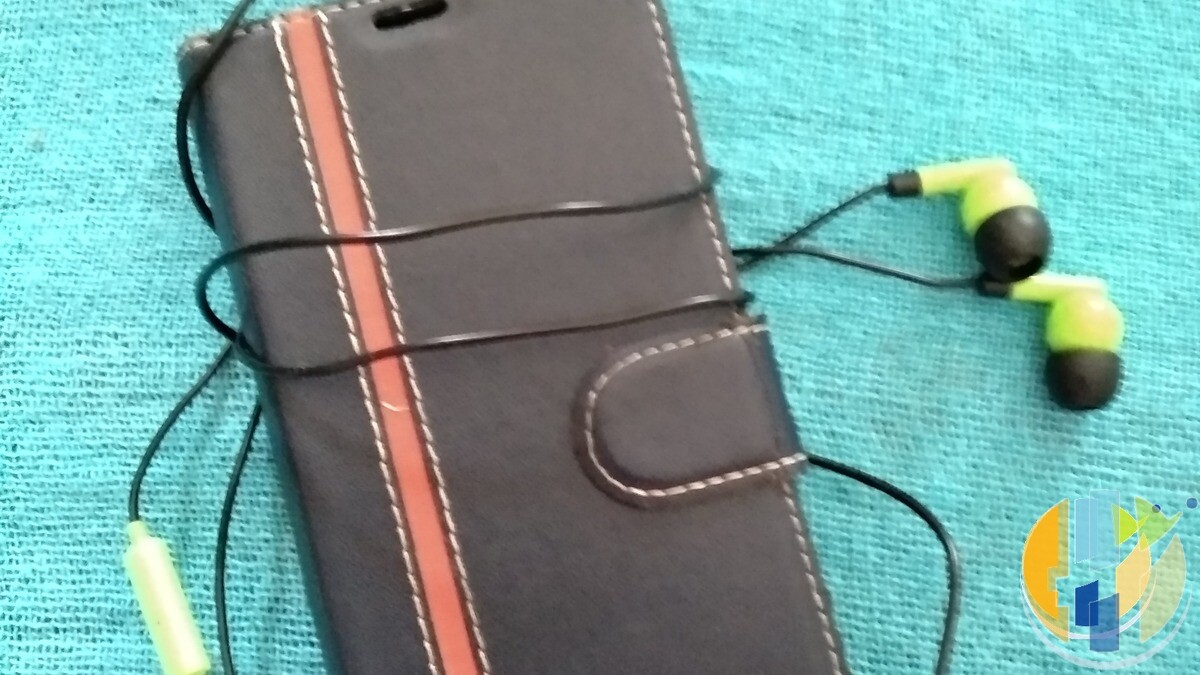 Real smartphone in a wallet case with neon wired earbuds on fabric — phone + earbuds kit for mobile streaming, no Vodafone marks.
