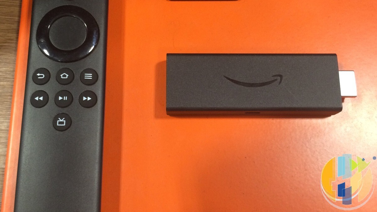 Real Amazon Fire TV Stick and Alexa Voice Remote on an orange display surface — everyday competing streaming stick + remote for UK stick-comparison context.