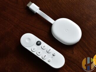 White Chromecast with Google TV and its voice remote on a dark wooden table