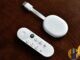 White Chromecast with Google TV and its voice remote on a dark wooden table
