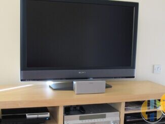 Sony BRAVIA TV on a light wood TV unit with a silver Sony AV receiver, PlayStation 3 and recorder on the shelves below