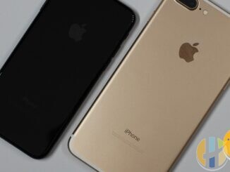 Jet black iPhone 7 and gold iPhone 7 Plus lying face down side by side on a light grey surface, showing their rear cameras and Apple logos