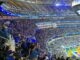Los Angeles Rams fans in blue and yellow shirts packing the stands at SoFi Stadium during a home game, with the SoFi Stadium video board above and the field in the corner