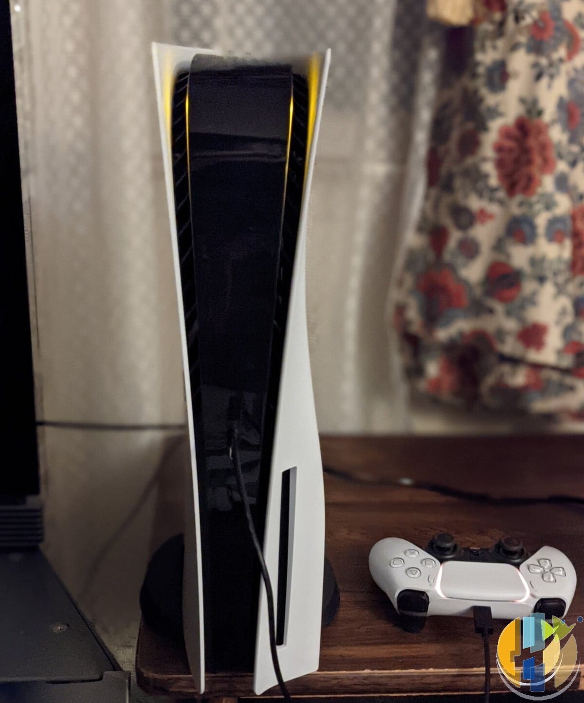 White PlayStation 5 console standing upright beside a DualSense controller on a wooden TV unit