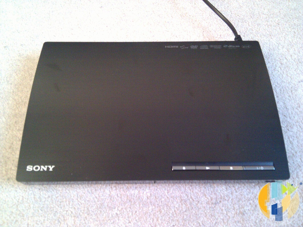 Slim black Sony Blu-ray player from around 2011 lying on a beige carpet with its power cable attached